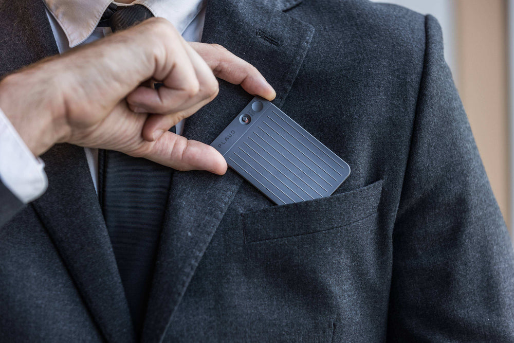 Person placing a Plaud note recorder into the pocket of a dark suit jacket.