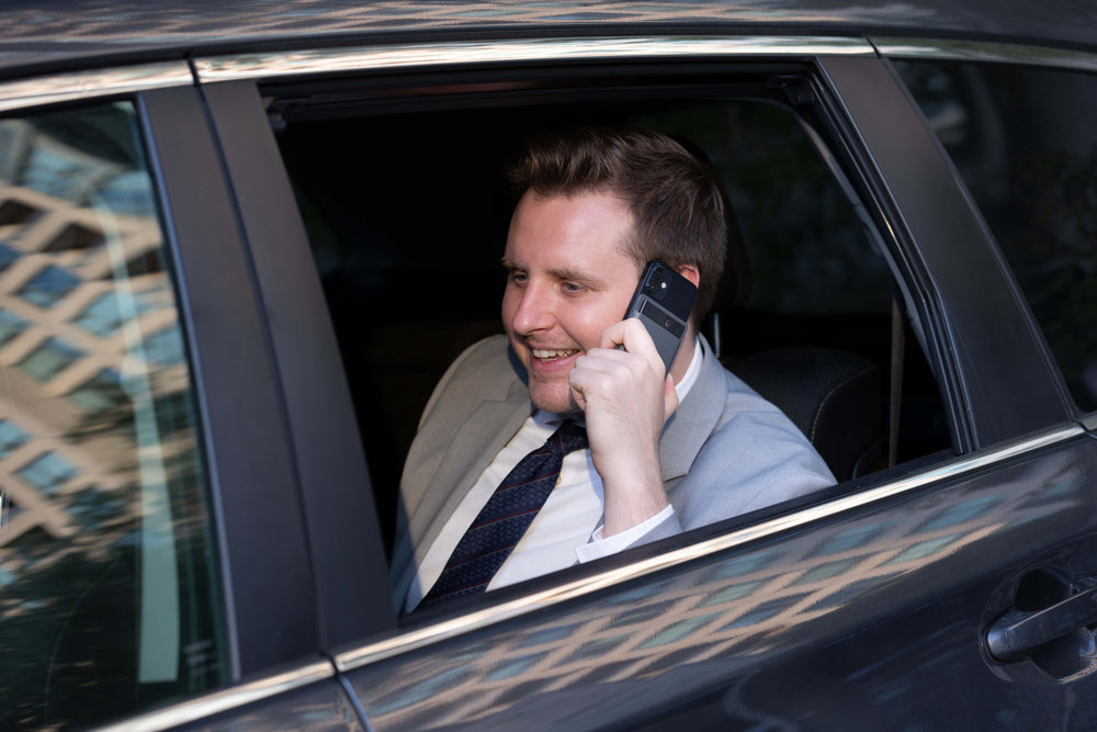 Man in a suit talking on a phone inside a car with plaud note recorder