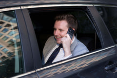 Man in a suit talking on a phone inside a car with plaud note recorder