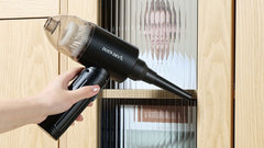 a handhold small vacuum is cleaning the bookshelf