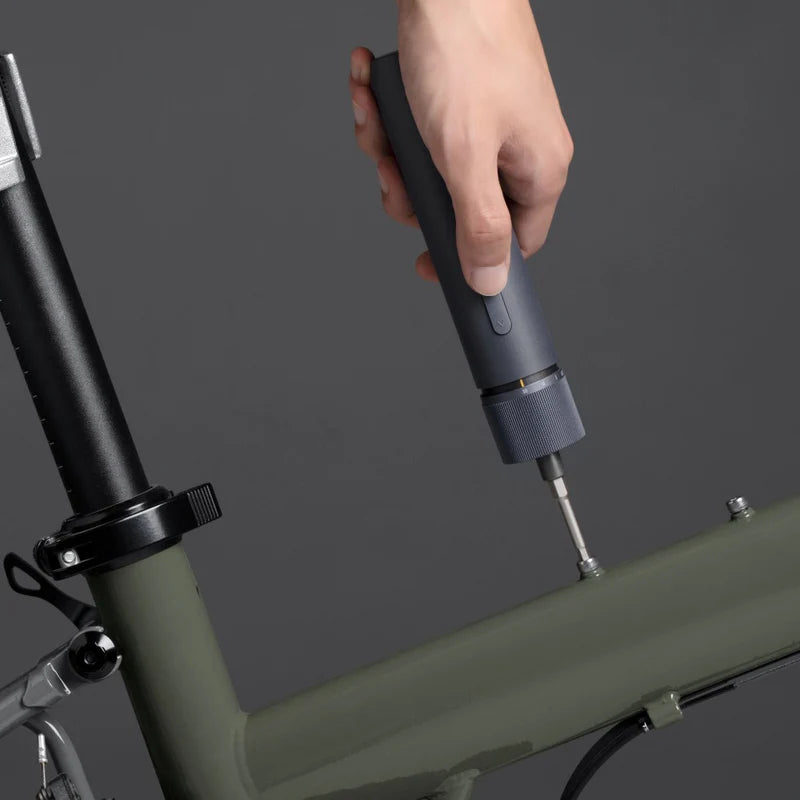 Hand using a tool on a bicycle frame against a dark background