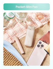 Pocket-slim fan on a surface with a phone, bottle, and other items.