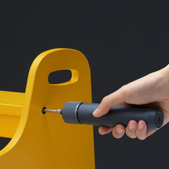 Hand using a black screwdriver on a yellow object against a dark background
