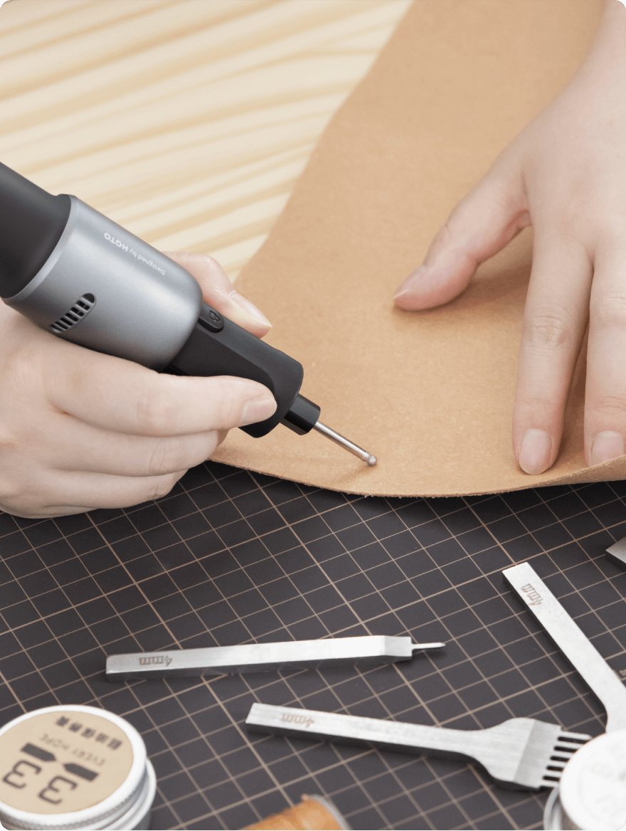 Person using a hot knife on leather with tools and a cutting mat in the foreground