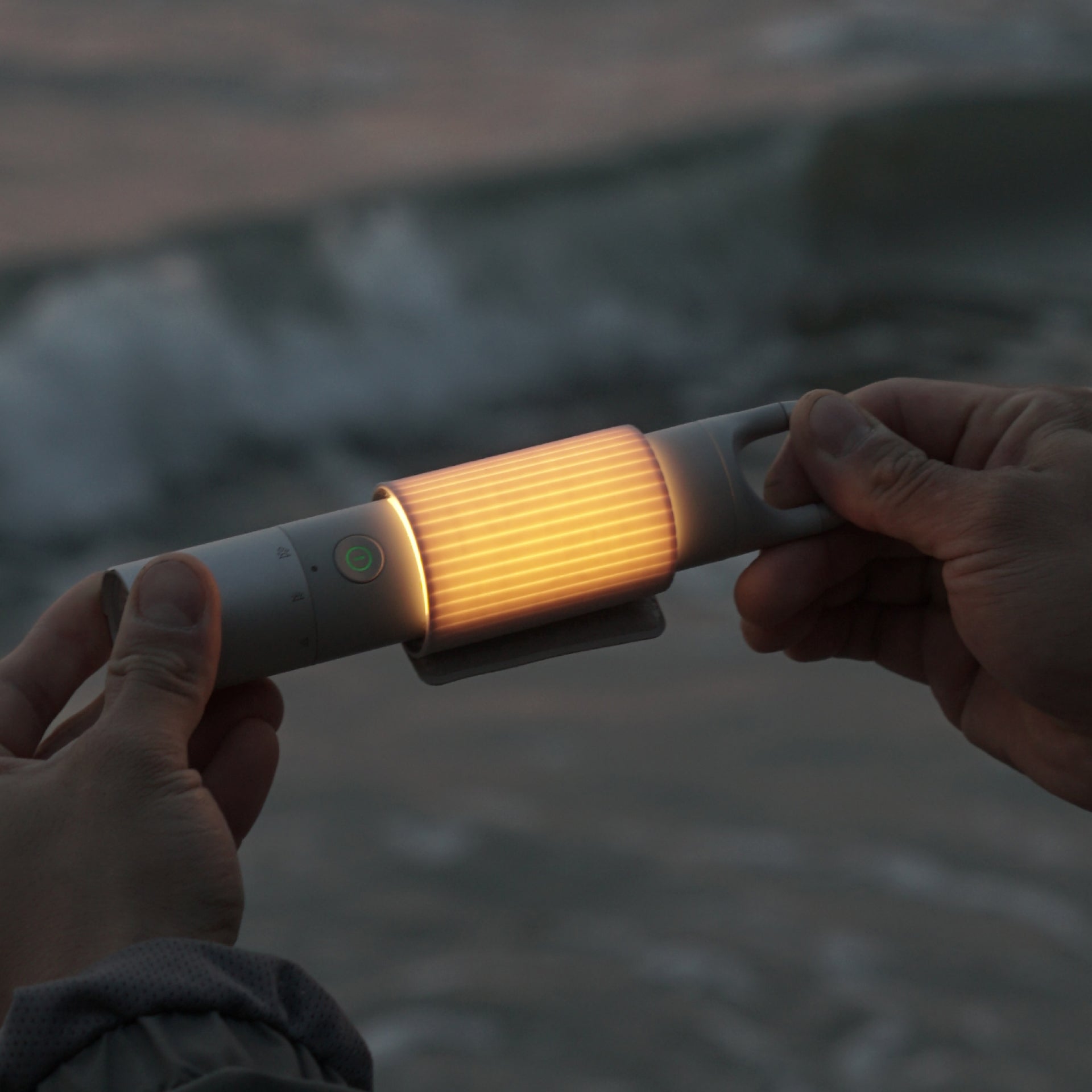 Two hands holding a glowing flashlight against a blurred natural background