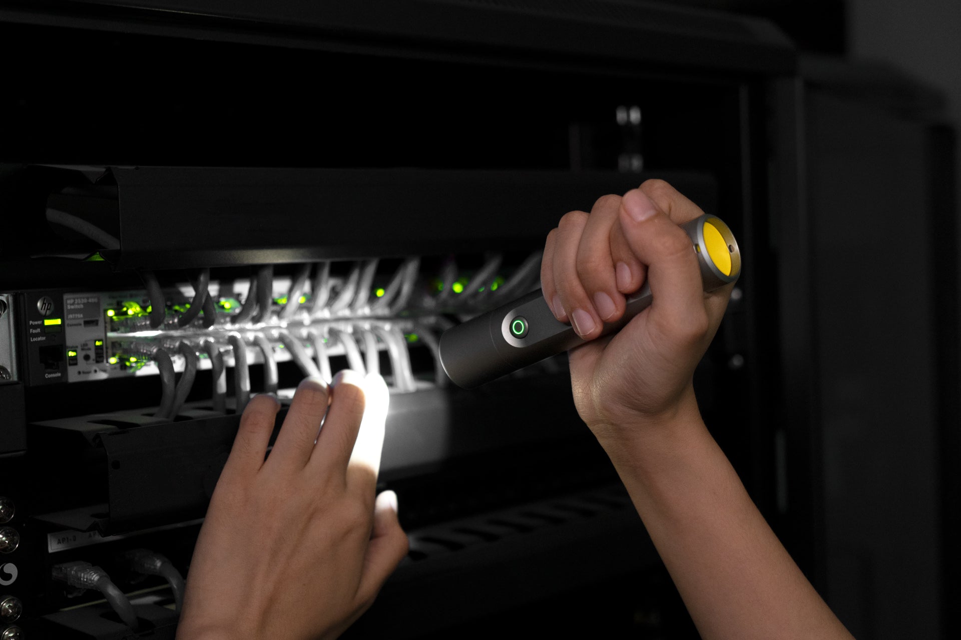 Person using a flashlight to inspect electronic equipment in a dark setting