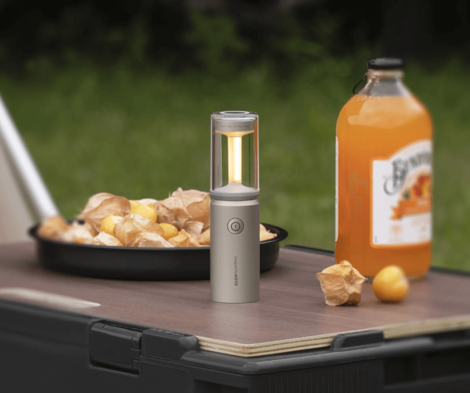 Portable lantern on a camping table with food and a bottle of juice.