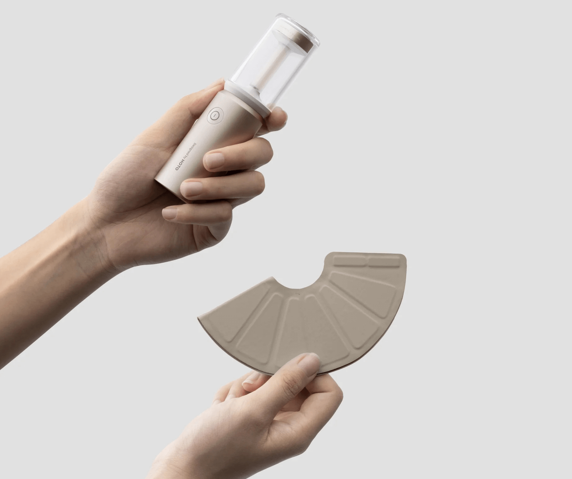 Hand holding a white handheld device with a beige fan-like component against a light gray background