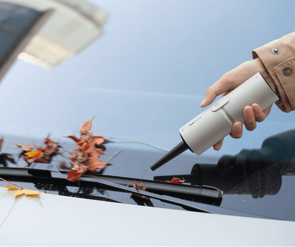 Person using a white vacuum cleaner to remove leaves from a car window