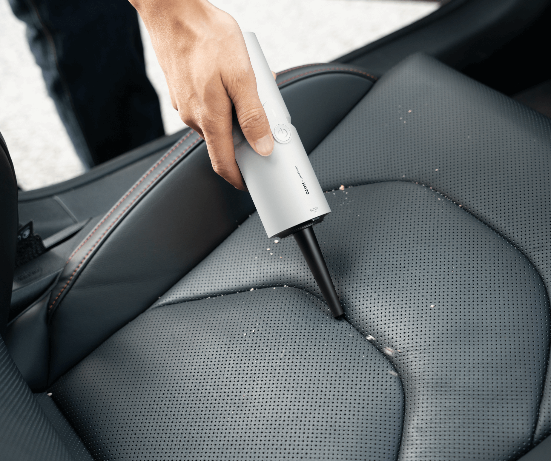 Person cleaning car seat with a handheld vacuum cleaner