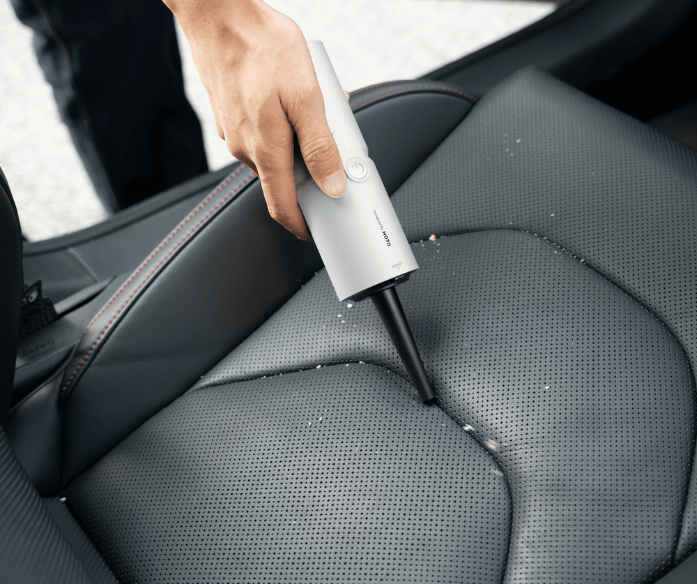 Person cleaning car seat with a handheld vacuum cleaner