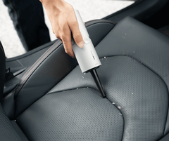 Person cleaning car seat with a handheld vacuum cleaner