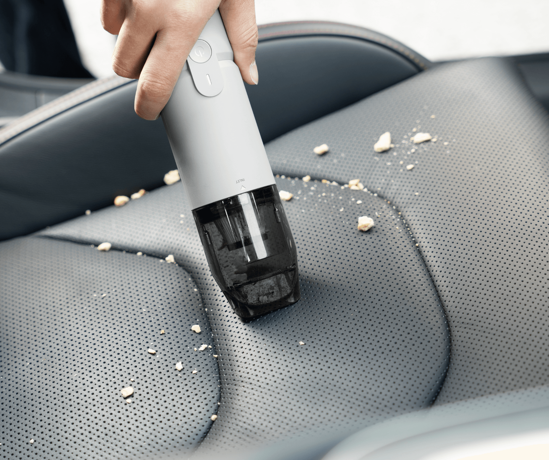 Hand using a handheld vacuum cleaner to clean a car seat.
