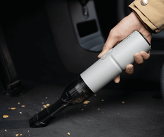 Hand holding a white handheld vacuum cleaner on a dark surface