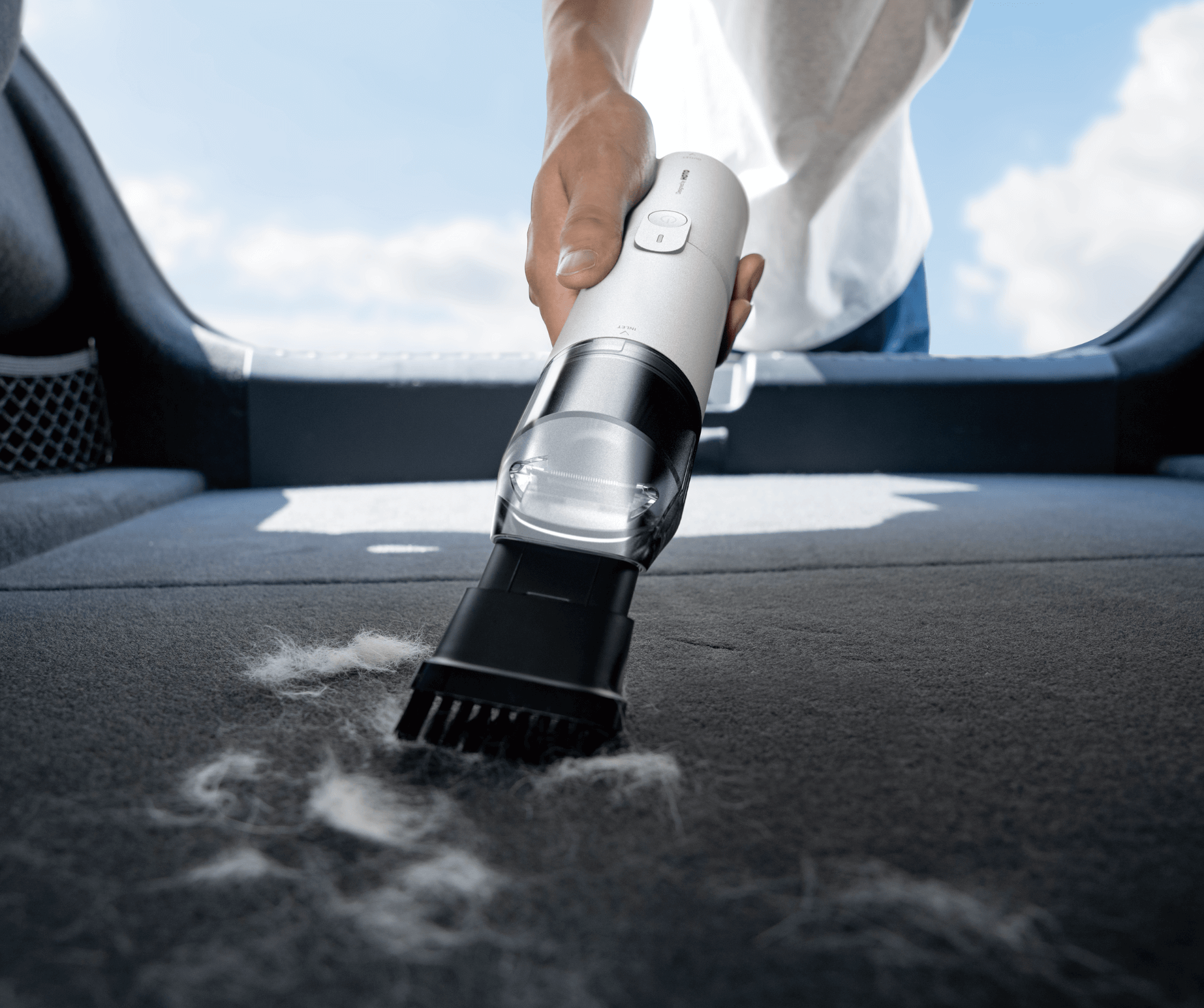 Person using a handheld vacuum cleaner to clean the interior of a car.