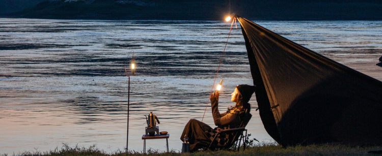 Person sitting in a hammock by a lake at night, holding a lantern.