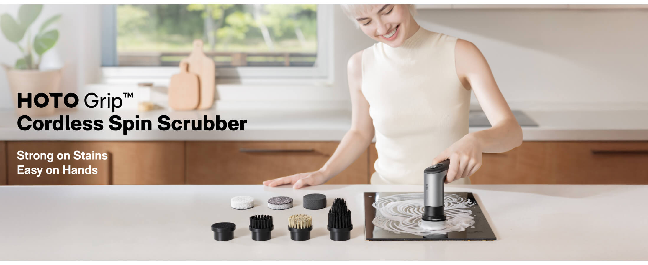 Woman using a cordless spin scrubber in a kitchen with various attachments displayed.