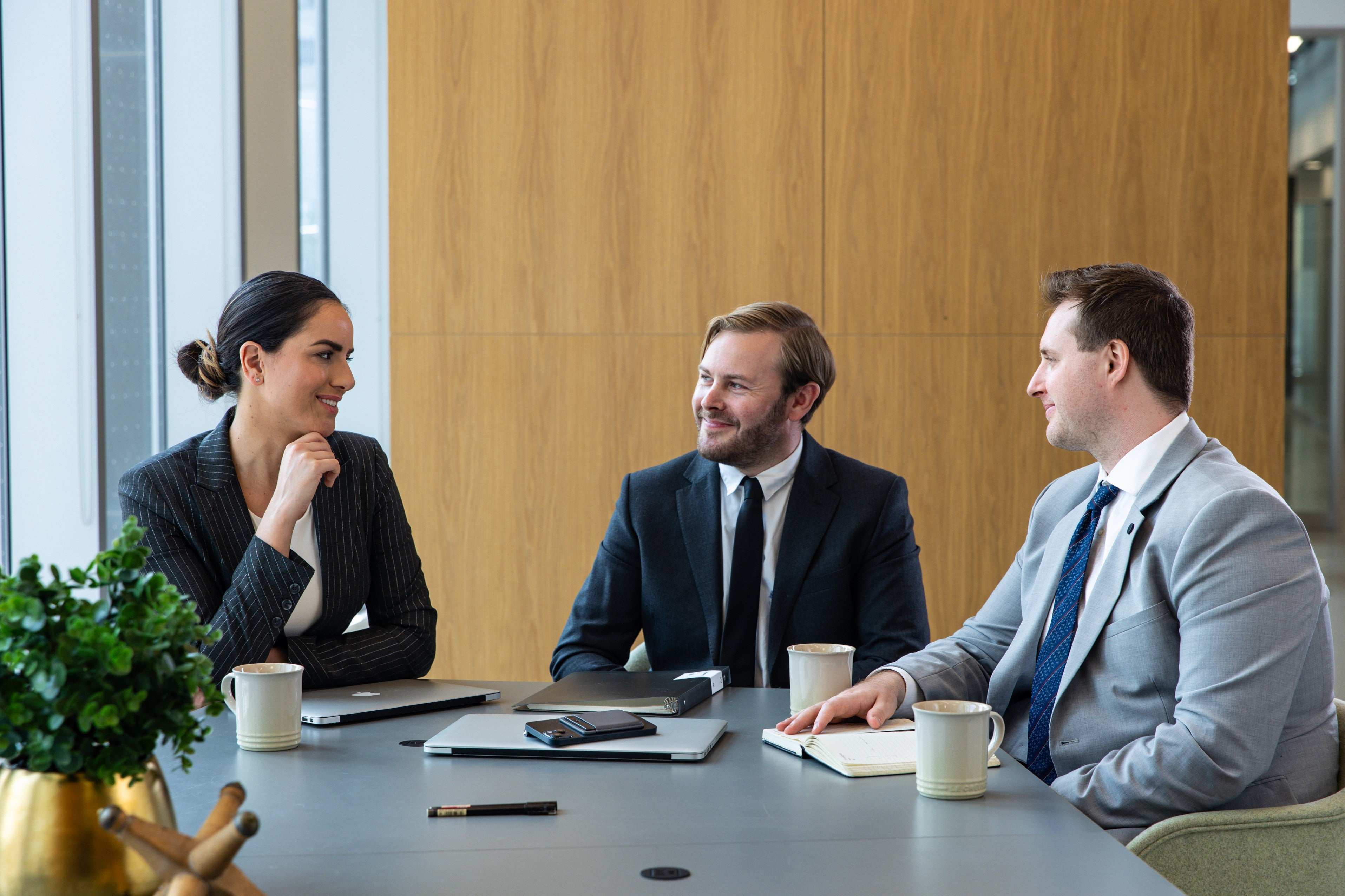 Three professionals in a meeting room discussing work with Plaud Note recording the meeting